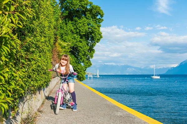 Zewnątrz portret ładny małej dziewczynki na rowerze obok pięknego jeziora w piękny słoneczny dzień — Zdjęcie stockowe