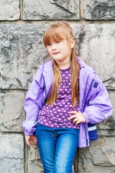 Retrato ao ar livre de uma bela menina pré-escolar vestindo jeans, top roxo e casaco de chuva — Fotografia de Stock