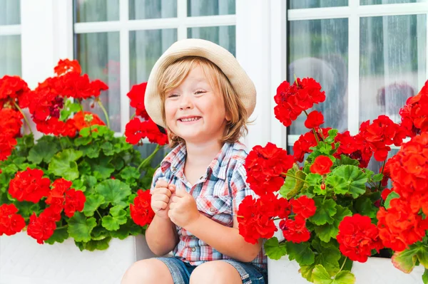 Verão retrato de uma criança bonito menino sentado entre bela vermelho Begonias — Fotografia de Stock