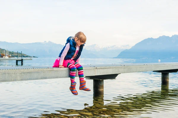 Außenporträt eines süßen kleinen Mädchens, das auf einem Steg sitzt — Stockfoto