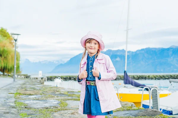 Outdoor portrait of a cute little girl, wearing pink vinyl rain coat and hat, colorful rain boots and pink tights — Stock Photo, Image