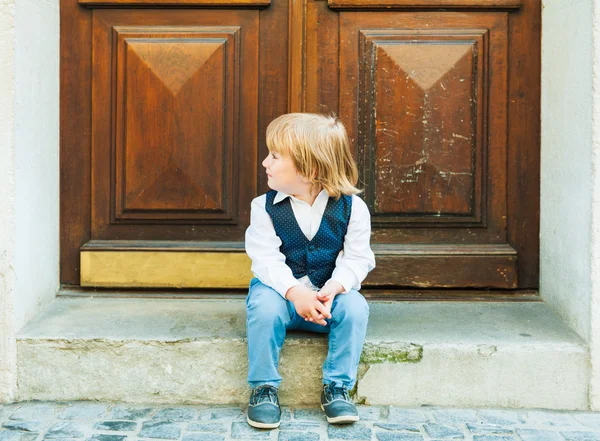 Retrato al aire libre de un lindo niño toodler, sentado en los escalones de una ciudad, vistiendo ropa hermosa celebración — Foto de Stock
