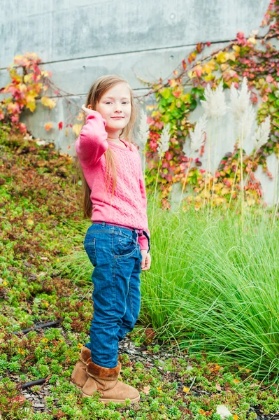 Retrato al aire libre de una linda niña en un jardín en un bonito día de otoño, con abrigo gris, jeans, jersey rosa — Foto de Stock