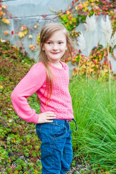 Retrato al aire libre de una linda niña en un jardín en un bonito día de otoño, con abrigo gris, jeans, jersey rosa —  Fotos de Stock