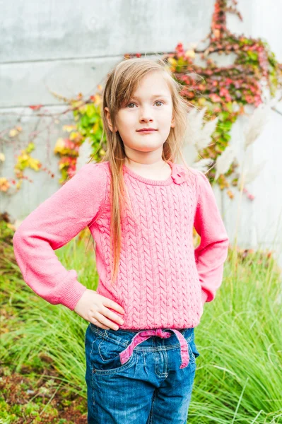 Retrato al aire libre de una linda niña en un jardín en un bonito día de otoño, con abrigo gris, jeans, jersey rosa — Foto de Stock