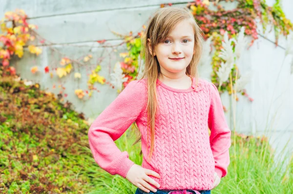 Ritratto all'aperto di una graziosa bambina in giardino in una bella giornata autunnale, con cappotto grigio, jeans, pullover rosa — Foto Stock