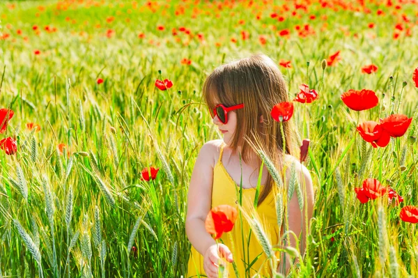 Summer portrait of a cute little girl playing in a poppy field on sunset, wearing yellow dress — Stock Photo, Image