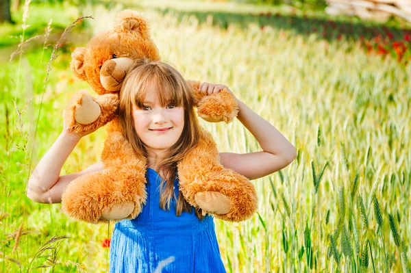 Latem portret śliczne małe dziewczyny zabawa z misiem w polu pszenicy — Zdjęcie stockowe