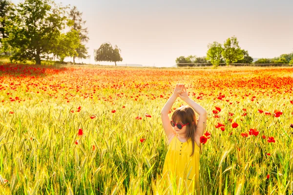 Summer portrait of a cute little girl playing in a pooppy field on sunset, wearing yellow dress — Stock Photo, Image