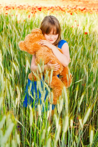 Summer portrait of a cute little girl playing with teddy bear in a wheat field — Stock Photo, Image