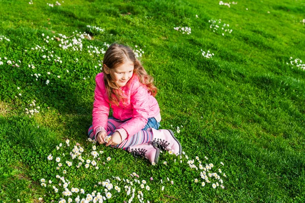 Beautiful little girl playing with flowers in a park on a nice sunny day in a early spring, wearing bright pink jacket — Stock Photo, Image