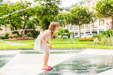 Bir çeşme ile güzel yaz gününde oynayan sevimli küçük kız