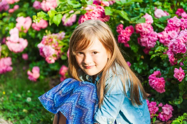 Retrato de uma menina bonita no pôr do sol, sentado ao lado de belos arbustos de rosa — Fotografia de Stock