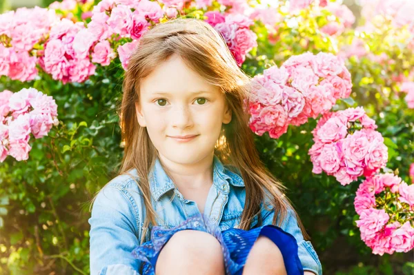 Sonnenuntergang Porträt eines netten kleinen Mädchens, das neben schönen Rosensträuchern sitzt — Stockfoto