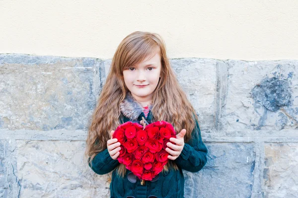 Birçok küçük gül ile yapılmış büyük kırmızı ahşap kalp tutan güzel küçük kız — Stok fotoğraf