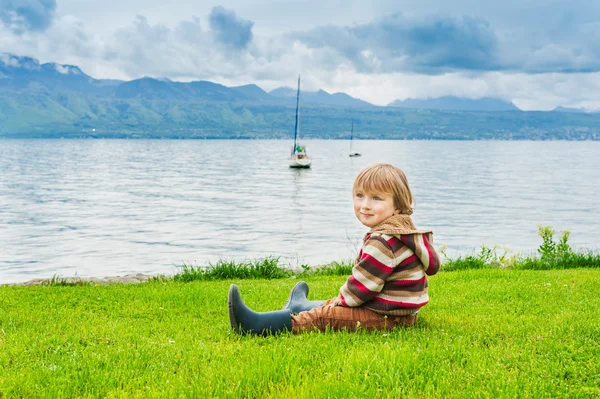 Bedårande barn pojke vila vid sjön en mulen dag — Stockfoto