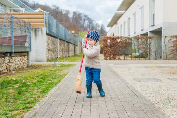 Arka bahçede bir erken bahar gününde süpürme şirin küçük çocuk — Stok fotoğraf