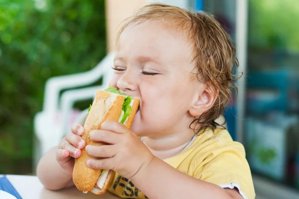 Menino pequeno comendo um sanduíche em um terraço em um belo dia de verão — Fotografia de Stock