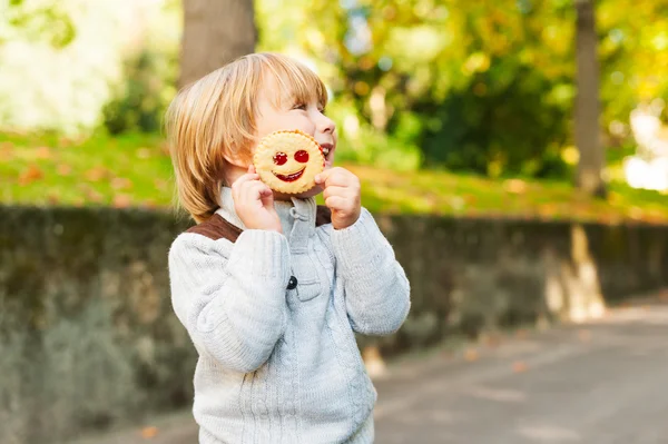 Outdoor portrait of adorable toddler boy in autumn park, having fun and eating a biscuit — Stock Photo, Image