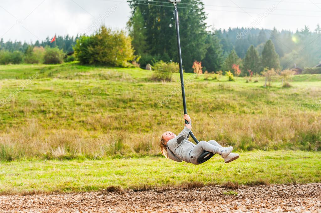 Cute toddler boy playing on a chain swing, having fun in a park on a nice autumn day