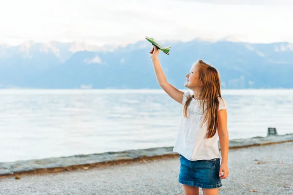 Yanında güzel göl günbatımı üzerinde duran ve bir küçük oyuncak uçak ile oynayan sevimli küçük kız — Stok fotoğraf