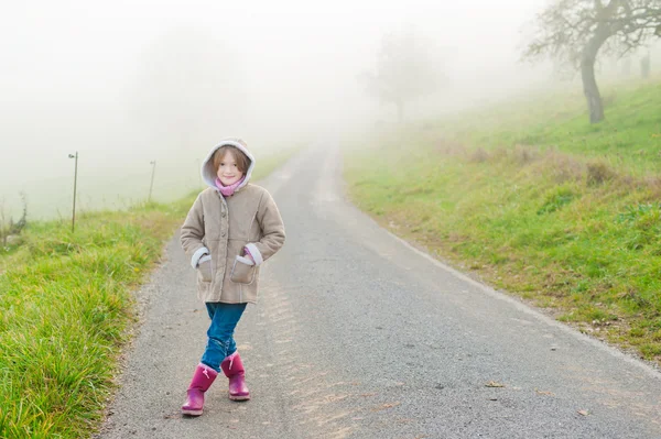Открытый портрет милой маленькой девочки в сельской местности в туманный день, в теплом бежевом пальто — стоковое фото