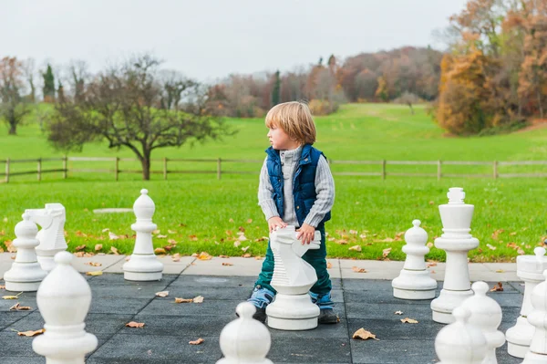 Adorable toddler boy playing with huge chess in a park on a cold day — Stock Photo, Image