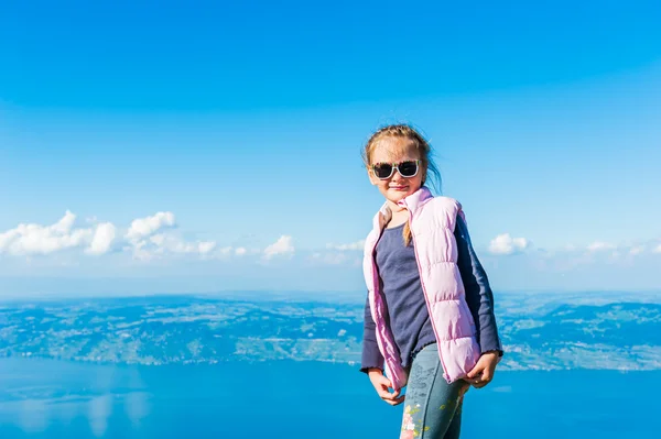 Roztomilá holčička, odpočívá na vrcholu hory a při pohledu na krásné jezero — Stock fotografie