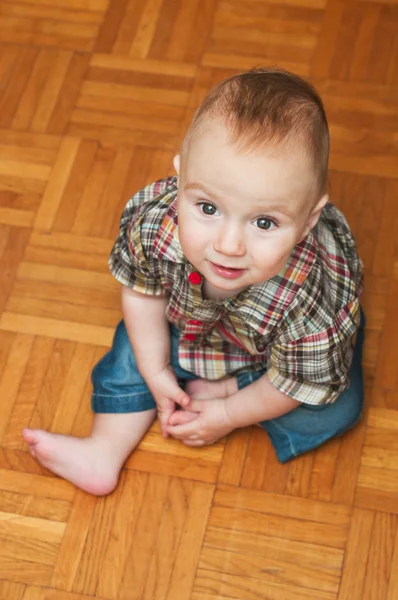 Retrato interior de um menino bonito sentado no chão de madeira em casa — Fotografia de Stock