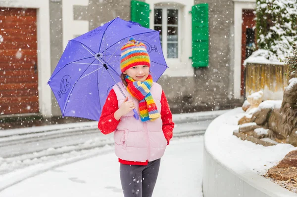 Utomhus porträtt av en söt liten flicka i en stad under snöfall — Stockfoto