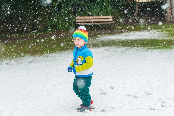 Χειμώνα πορτρέτο του χαριτωμένο μικρό αγόρι στο πλαίσιο της χιονόπτωσης, φορώντας πουλόβερ Χριστούγεννα και πολύχρωμο καπέλο — Φωτογραφία Αρχείου
