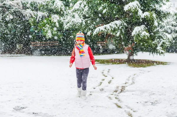 Zimní portrét roztomilá holčička za sněžení, nosí červený svetr, barevný klobouk a šátek — Stock fotografie