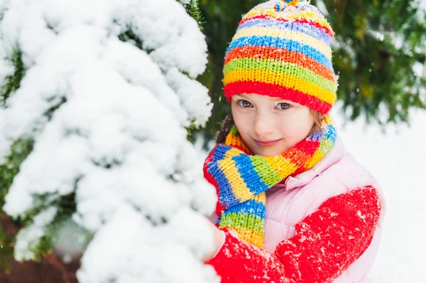 Vinter porträtt av en söt liten flicka under snöfall, klädd i röd tröja, färgglad mössa och halsduk — Stockfoto