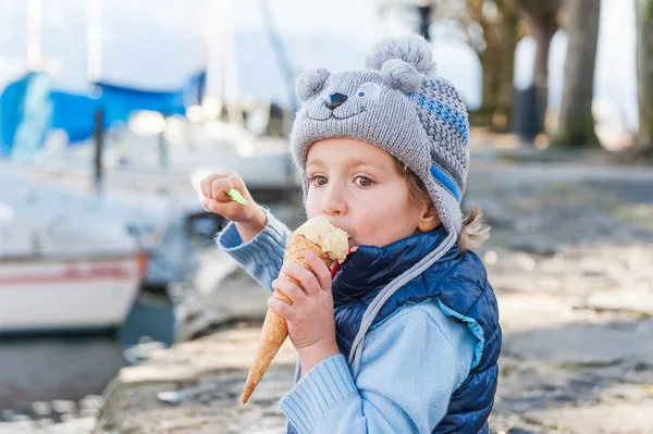 Menino adorável comendo sorvete ao ar livre em um tempo frio — Fotografia de Stock