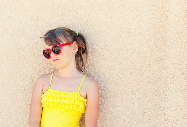 Ritratto di una graziosa bambina con occhiali da sole rossi e costume da bagno giallo — Foto Stock