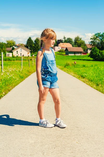 Portrait d'été d'une petite fille de 6 ans, portant des salopettes en denim et des chaussures grises , — Photo