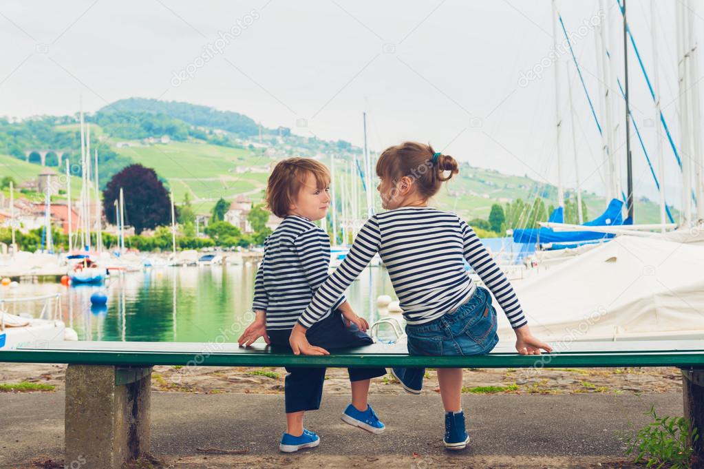 Two kids, little girl and boy resting by the lake, wearing frocks and blue shoes