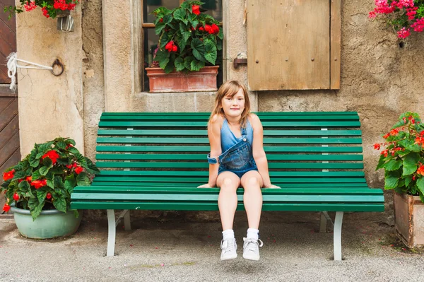 Zomer portret van een schattig klein meisje van zeven jaar oude zittend op de Bank in de tuin — Stockfoto