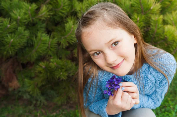 Close up portrait of a cute little girl, holding small bouquet of violets, wearing blue pullover — Stock Photo, Image