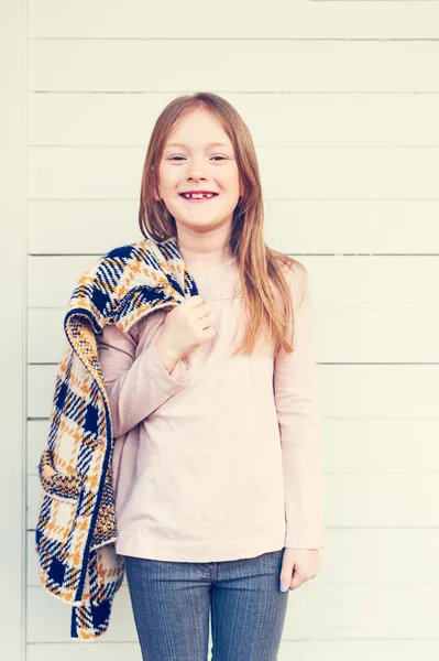 Fashion portrait of a cute little girl of 7 years old, wearing pink shirt, holding yellow and blue plaid cardigan, toned image — Stock Photo, Image