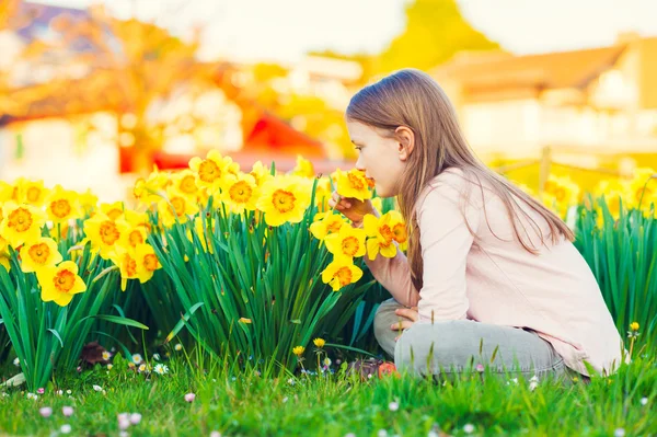 Bedårande liten flicka leker med blommor i parken vid solnedgången, att lukta påskliljor — Stockfoto