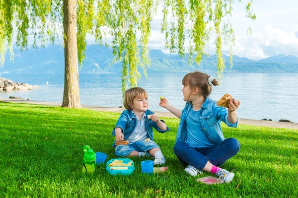 İki sevimli çocuk, küçük kız ve kardeşi göl kenarında piknik açık havada,