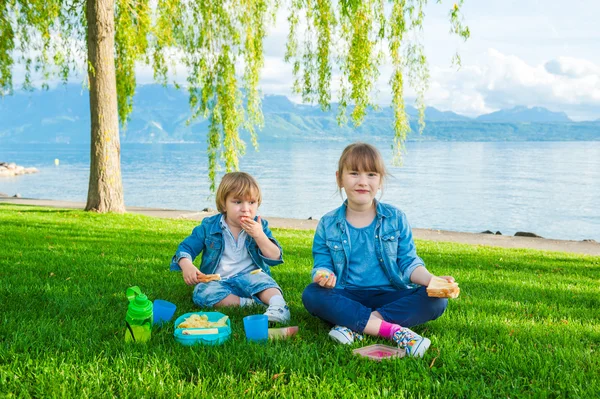 Två söta barn, liten flicka och hennes bror, har picknick utomhus vid sjön — Stockfoto