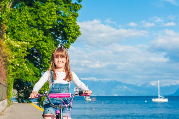 Cute little girl riding on a bicycle by the lake — Stock Photo, Image