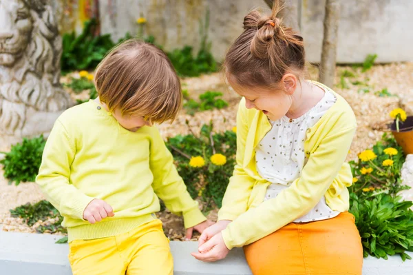 Duas crianças bonitas brincando ao ar livre, vestindo roupas amarelas — Fotografia de Stock