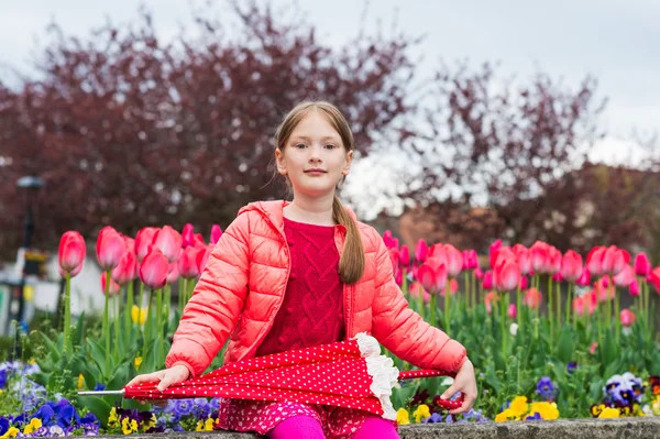 Utomhus porträtt av en söt liten flicka på 7 år gammal, bär ljusa rosa jacka, innehar paraply — Stockfoto