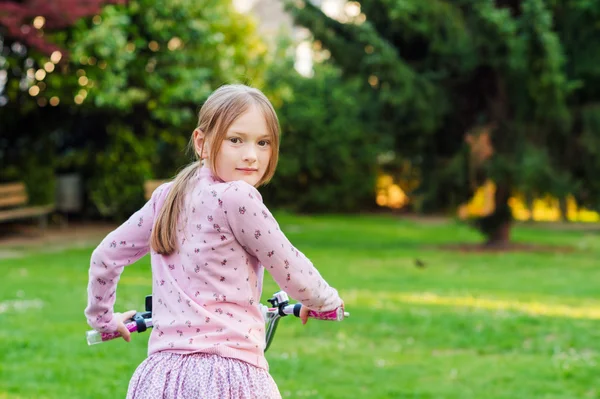 嘴甜的小姑娘，她的自行车在公园里回望越过她的肩膀上 — 图库照片