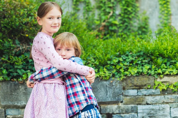 Outdoor portrait of two adorable kids, big sister and her little brother hugging each other — Stock Photo, Image