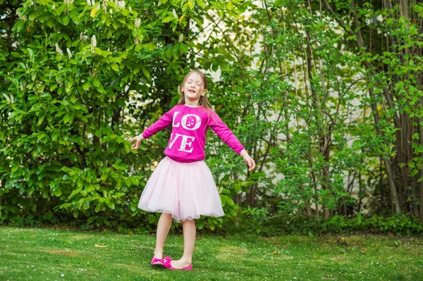 Adorable niña dando vueltas en un hermoso parque en un buen día, con falda de tutú, zapatos de bailarina y camiseta rosa brillante — Foto de Stock