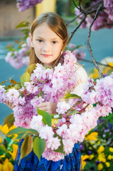 Portret wiosny cute dziewczynka gra o zachodzie słońca z kwiatami wiśni japońskiej w kwiat — Zdjęcie stockowe